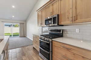 Kitchen featuring stainless steel appliances, lofted ceiling, light stone counters, backsplash, and wood finish floors