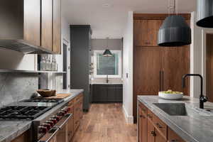 Dual tone kitchen with ventilation hood, stainless steel appliances, two tone cabinetry, dark stone countertops, and light wood-style flooring