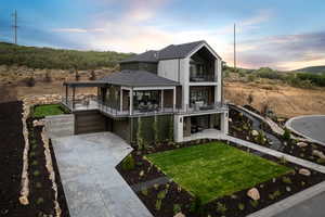 View of front of home with an attached garage, concrete driveway, a lawn, a balcony, and a patio area