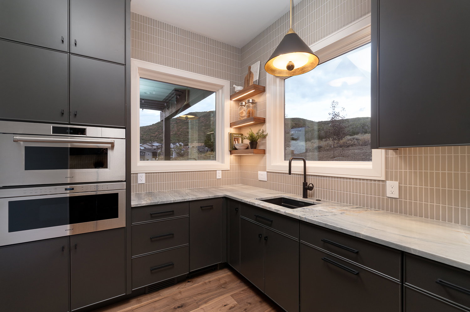 Dual tone kitchen featuring double oven, light stone countertops, hanging light fixtures, dark wood-type flooring, and dual tone cabinets