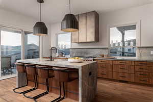 Kitchen featuring light stone counters, a kitchen breakfast bar, an island with sink, light wood-style flooring, and tasteful backsplash