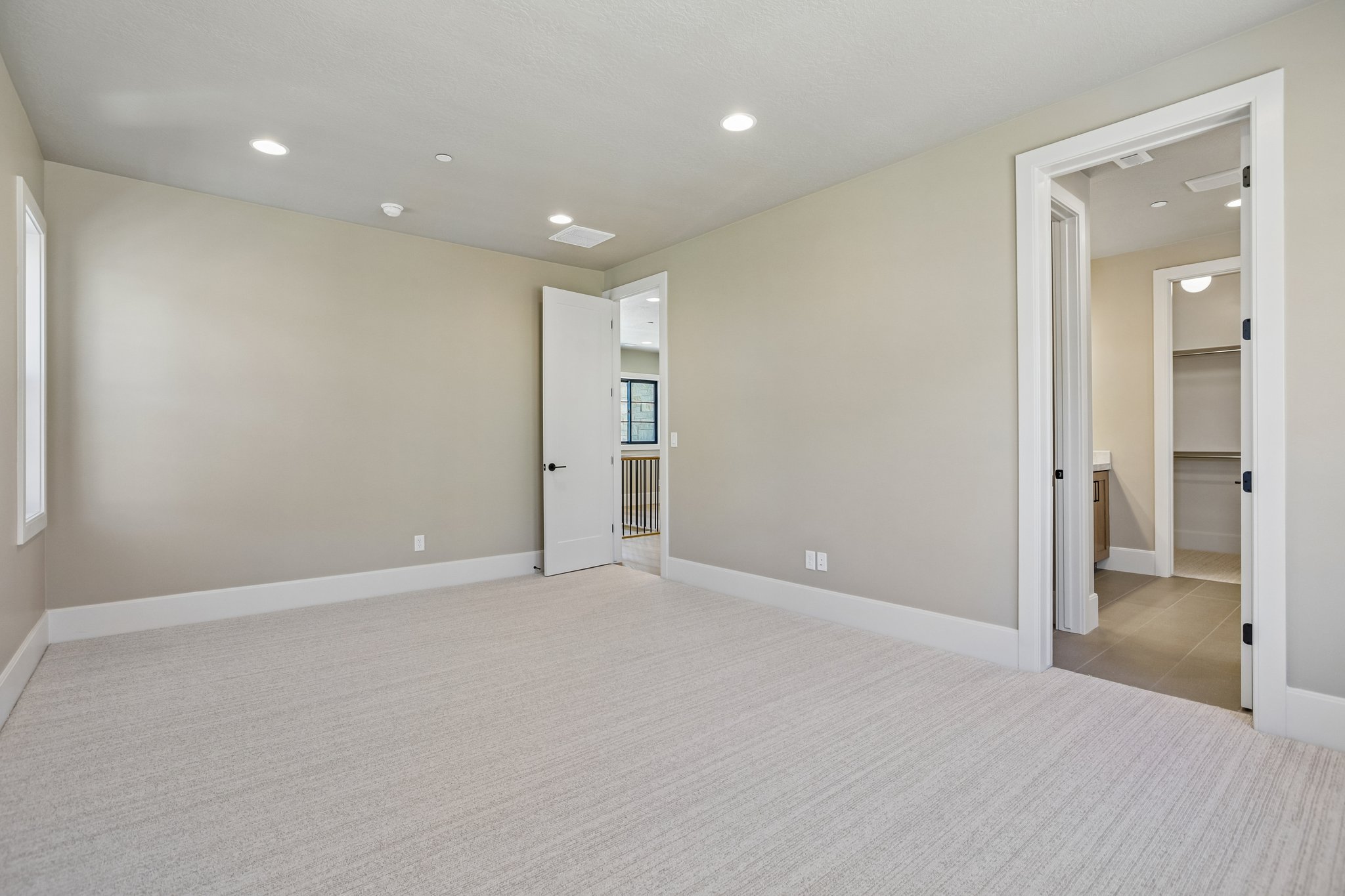 Spacious room featuring neutral carpeting, recessed lighting, and a window with white trim