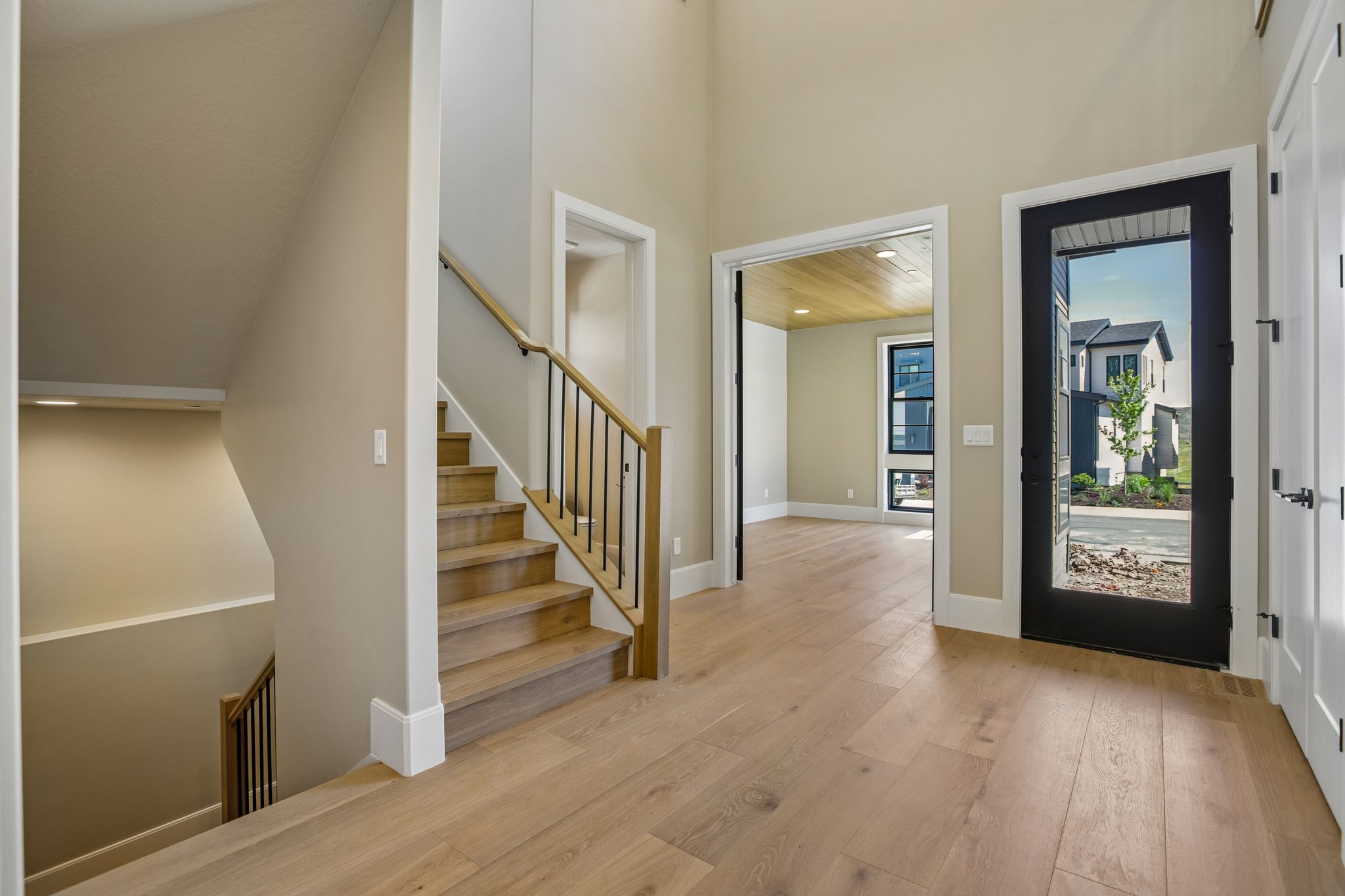 Entryway with wood-finish flooring, a contemporary staircase featuring wood handrails and black metal balusters, and a black-framed glass entry door