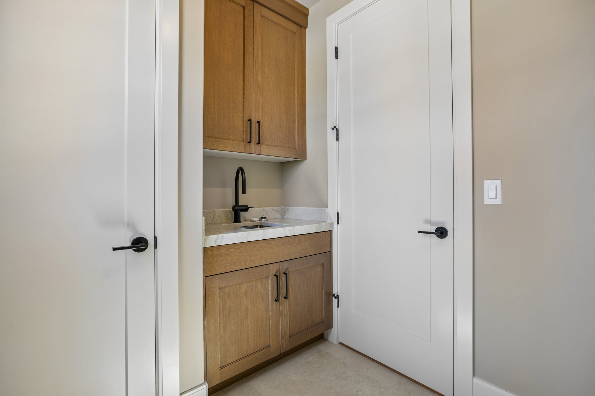 Utility sink area featuring light wood-finish cabinetry, a stone countertop, a matte black gooseneck faucet, and an undermount sink