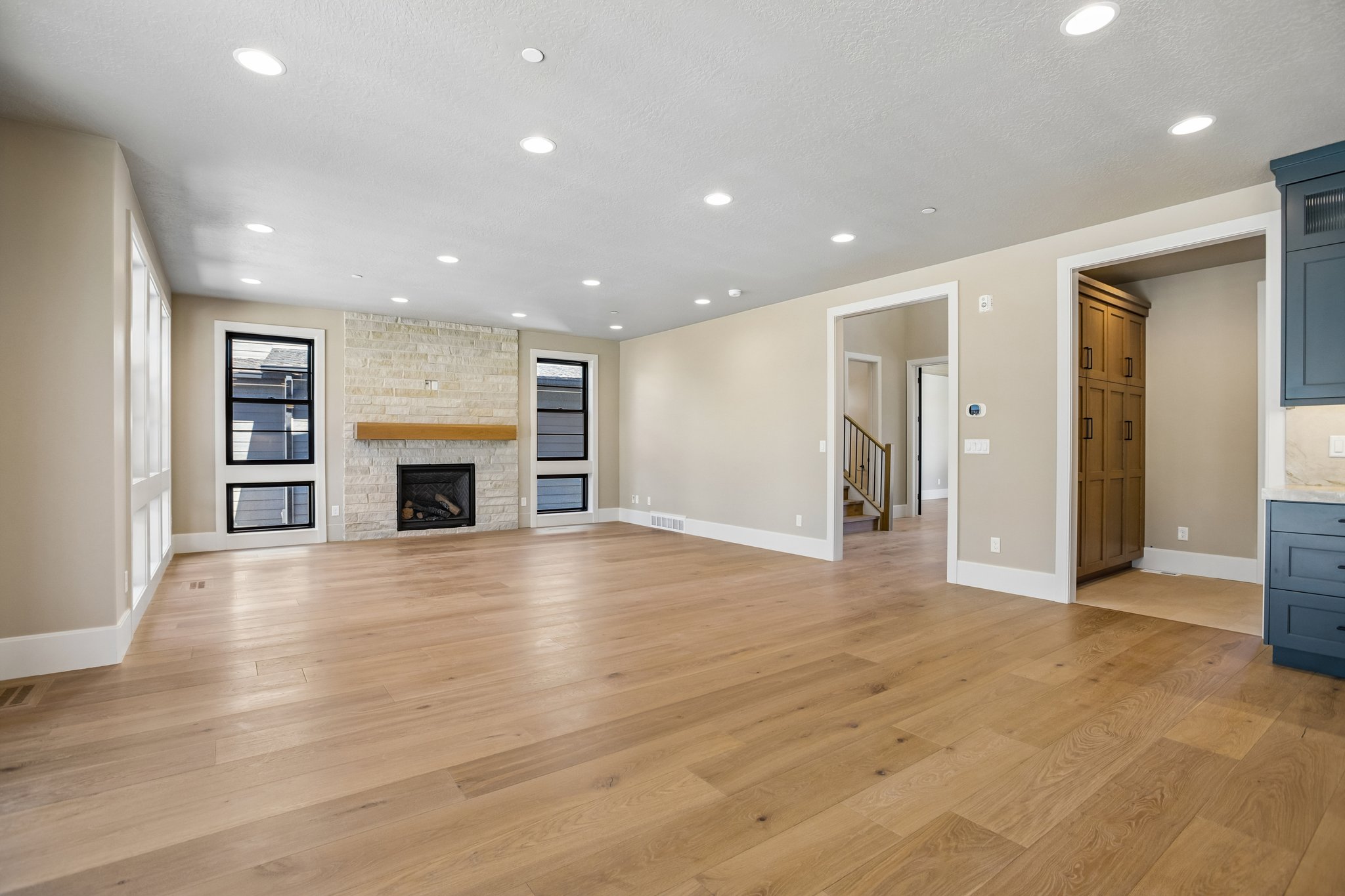 Spacious room featuring wide plank wood-finish flooring, a stone-clad fireplace with a wood mantle, and recessed lighting