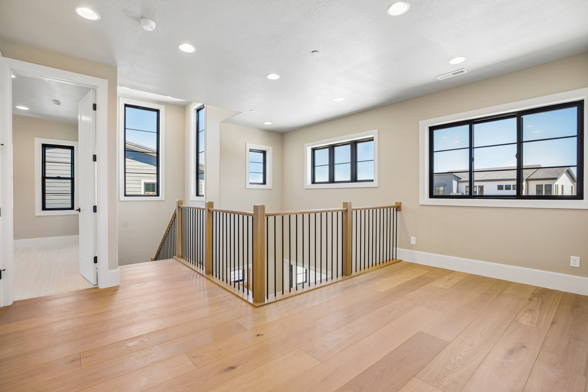 Hardwood flooring extends throughout this upper-level space featuring a contemporary wood and metal baluster railing, recessed lighting, and multiple black-framed windows