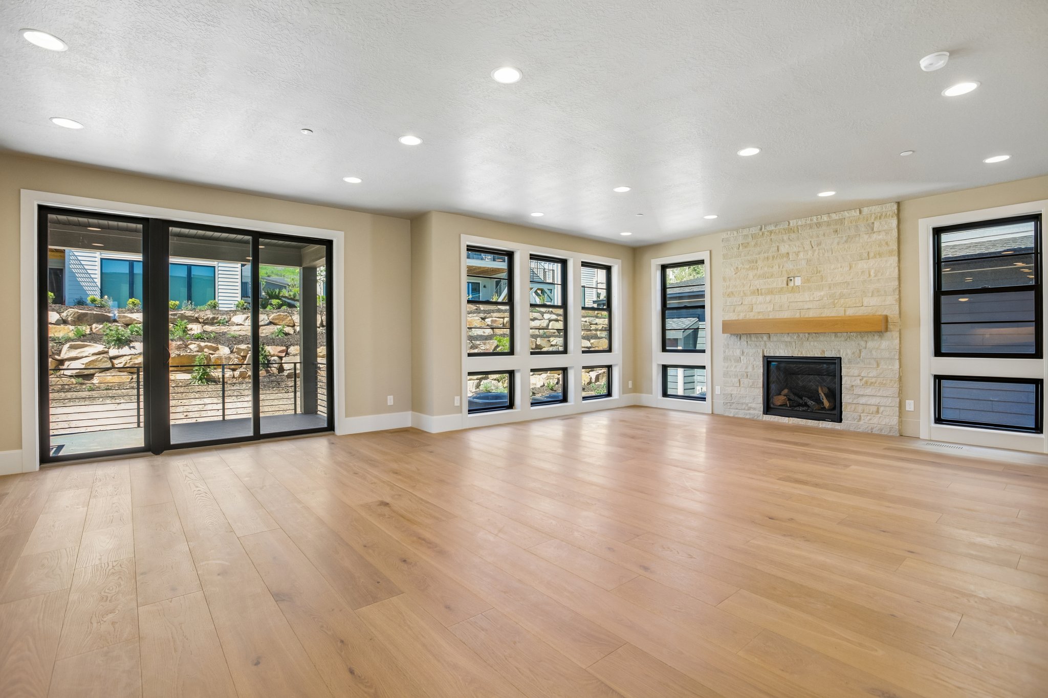 Open-concept living space featuring light wood-finish flooring, recessed lighting, and a stone-clad fireplace with a wood mantel