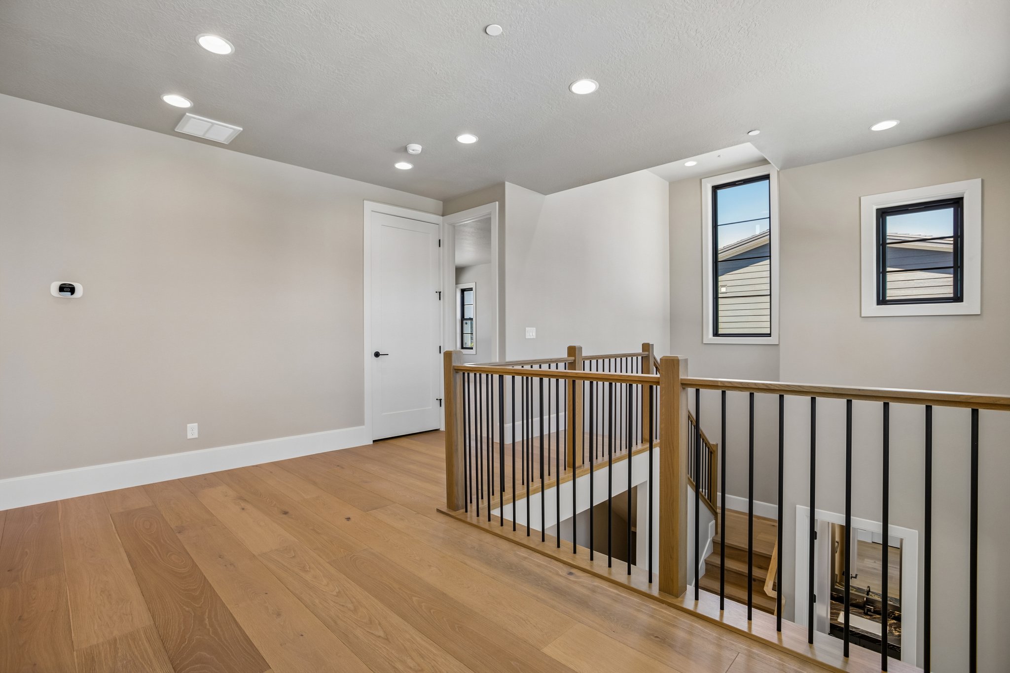 Upper-level landing featuring wood-finish flooring, recessed lighting, and a contemporary wood and iron railing