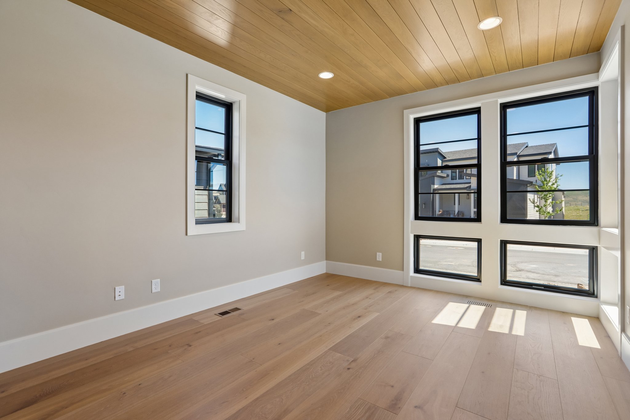 Spacious room featuring light wood-finish flooring, a wood-paneled ceiling, recessed lighting, and large windows with black frames