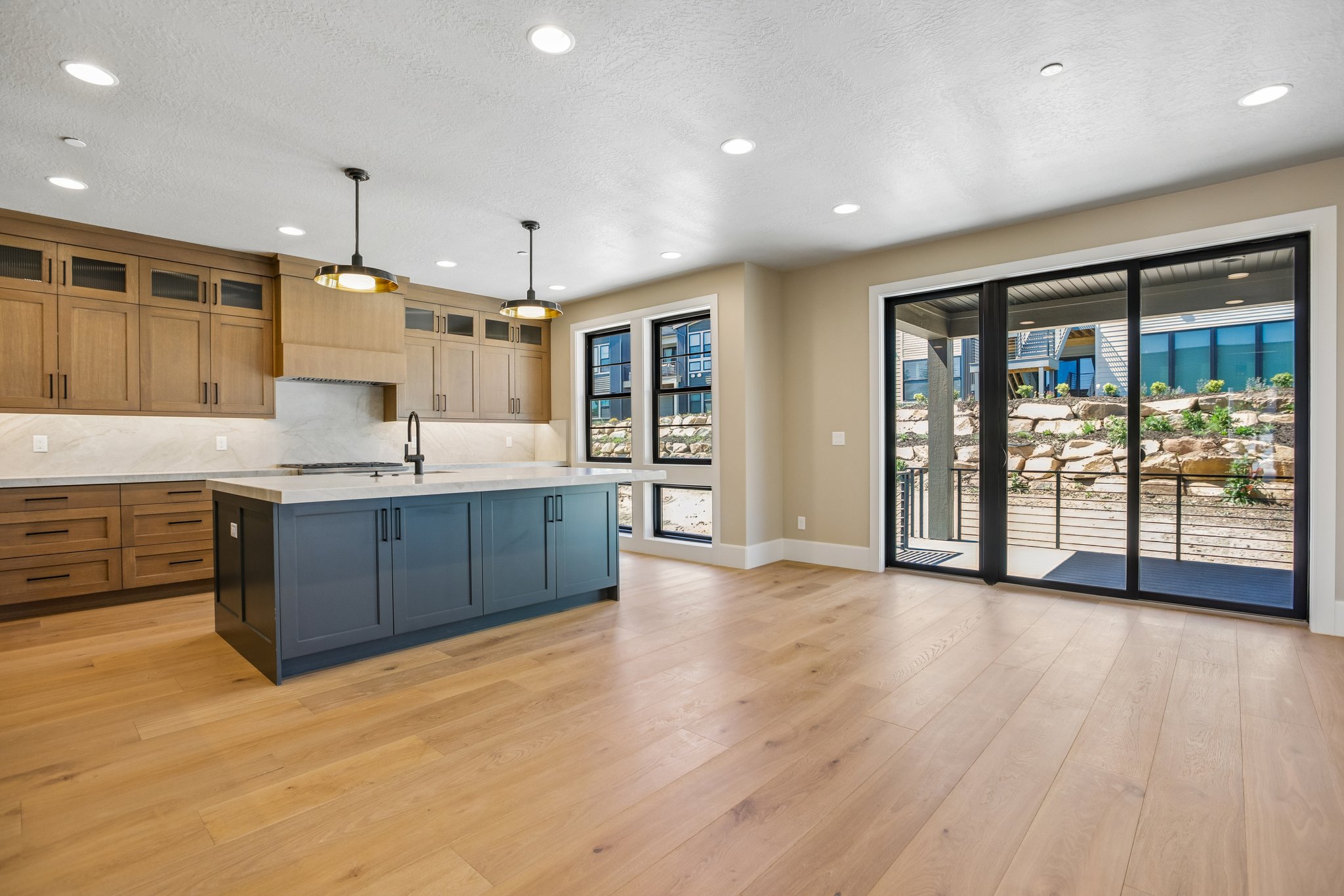 Open-concept kitchen and living area featuring wood-finish flooring, a large kitchen island with contrasting cabinetry, and a range hood