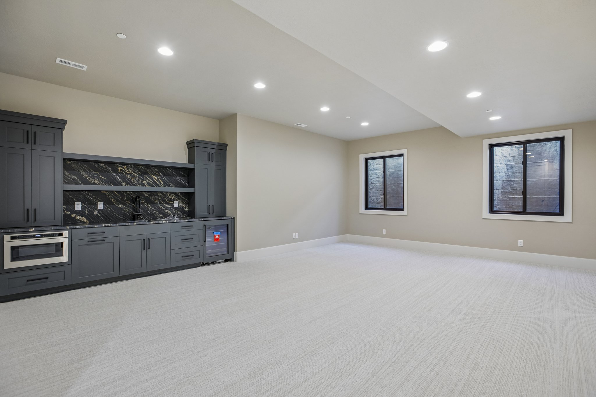 Spacious room featuring a built-in dark gray cabinetry unit with a black and gold patterned backsplash, integrated microwave, and beverage refrigerator