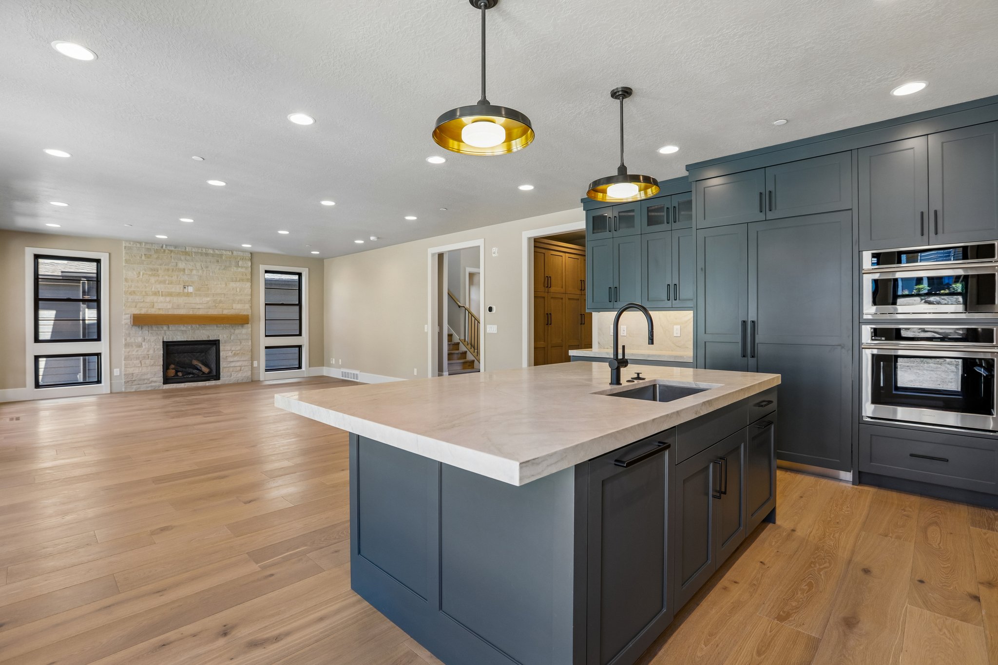 Gourmet kitchen featuring a large island with sink, integrated refrigerator, double wall ovens, extensive cabinetry, and wood-finish flooring