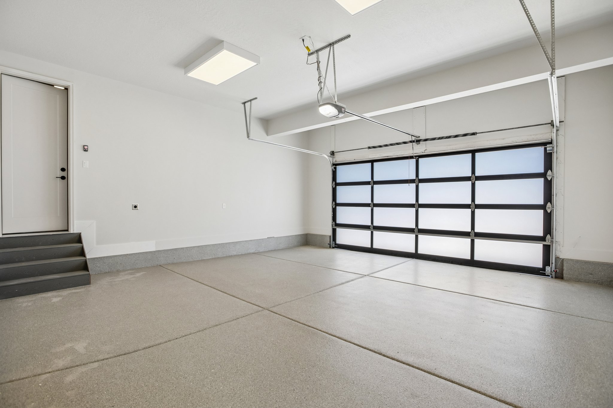 Spacious garage featuring a modern glass panel garage door, light gray epoxy flooring, white painted walls, and overhead lighting