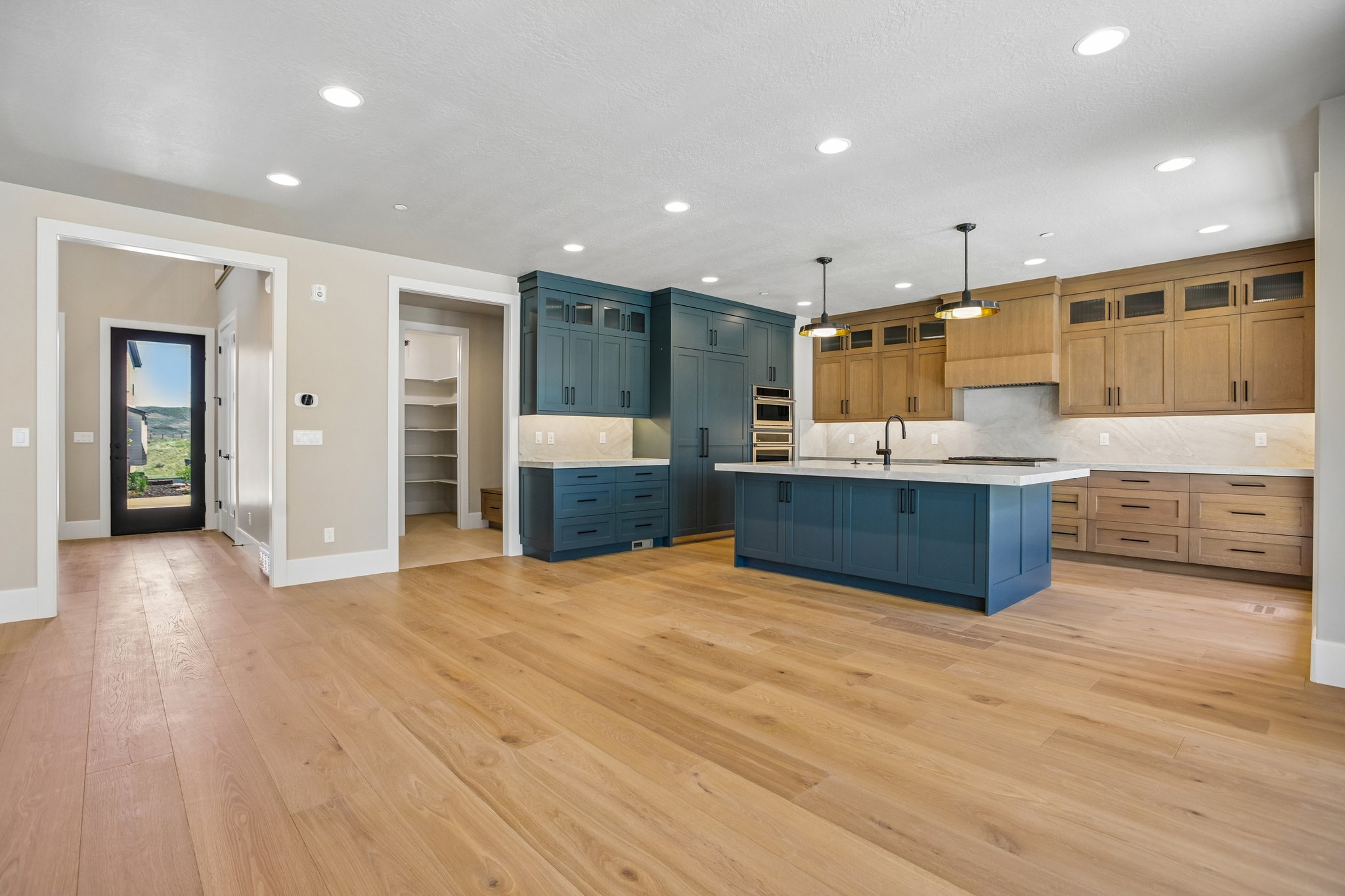 Open-concept kitchen featuring an oversized island with pendant lighting, integrated wall ovens, two-tone cabinetry, and wood-finish flooring