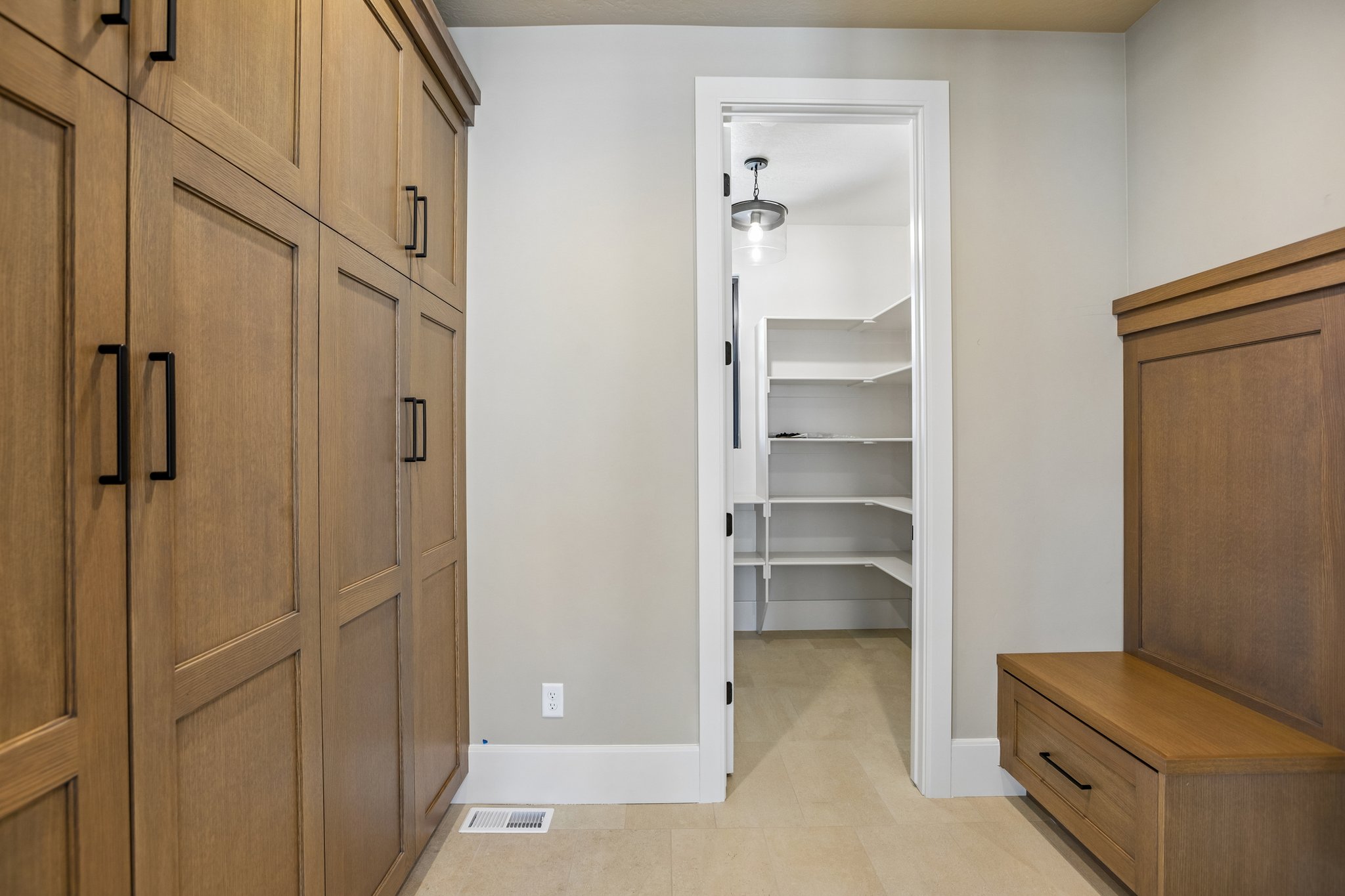 Entryway featuring extensive wood-finish cabinetry with matte black hardware, built-in bench with storage drawer, and access to a pantry with white shelving