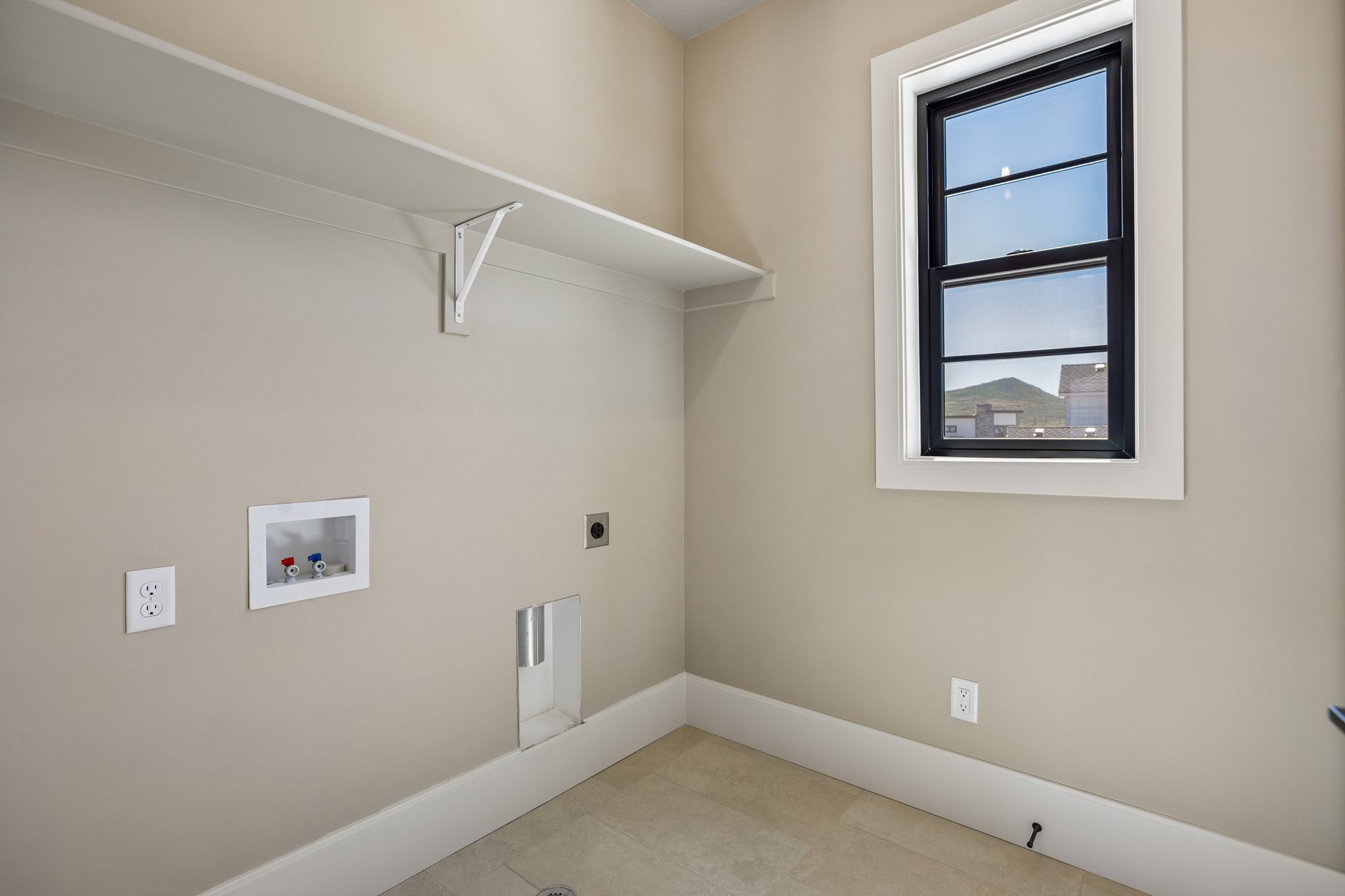 Utility room featuring a single window with black trim, tile flooring, wall-mounted shelving, and plumbing hookups