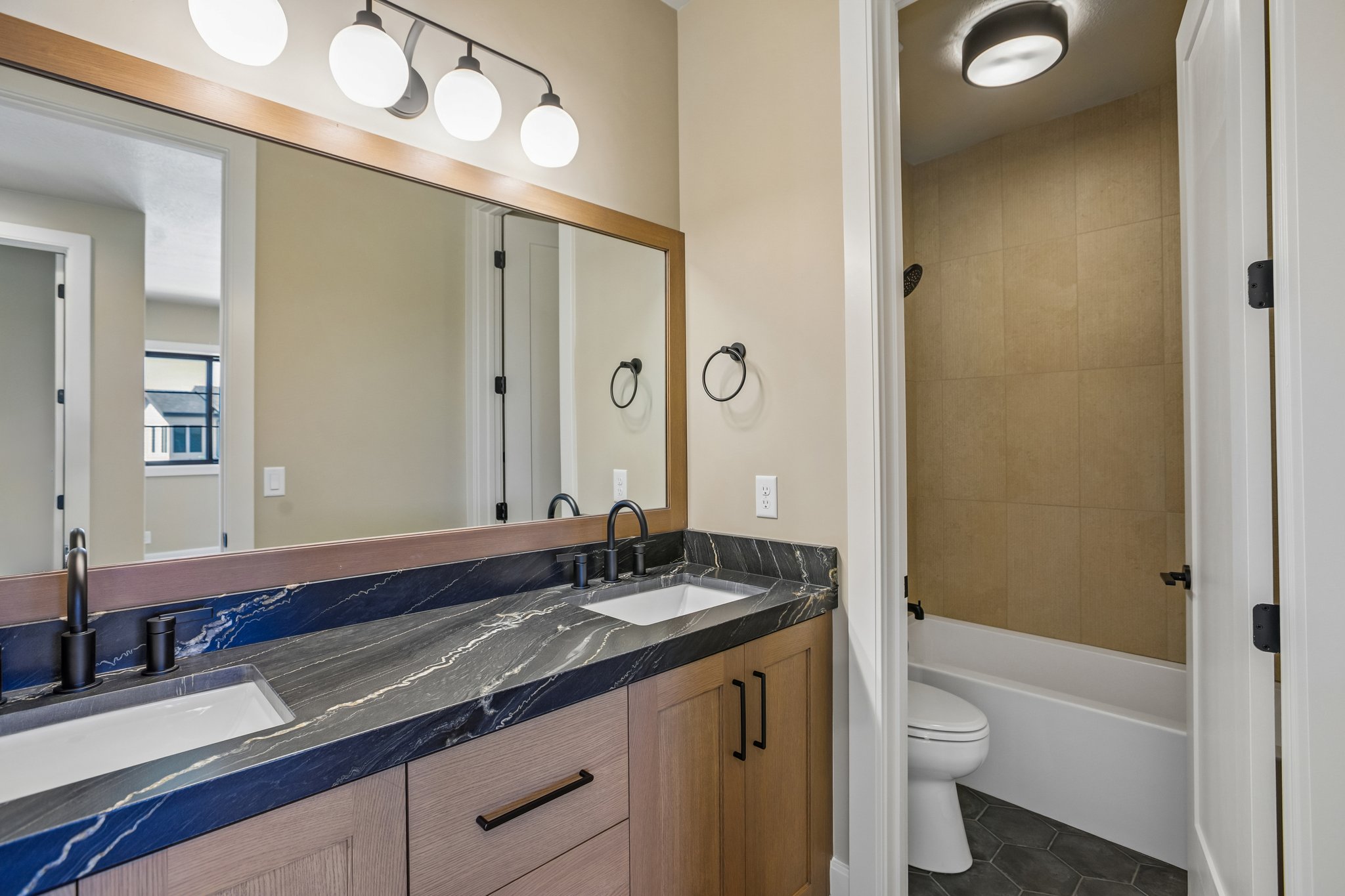 Dual vanity featuring wood-finish cabinetry, dark stone countertops with white undermount sinks, and matte black fixtures