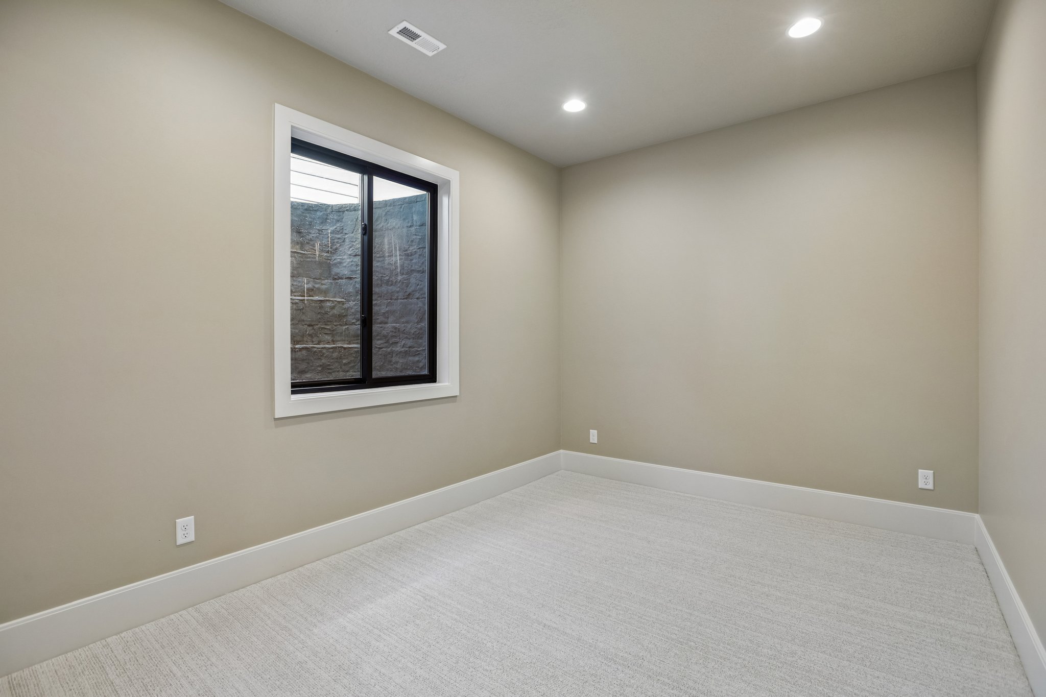 Bright room featuring a window with black trim, recessed lighting, neutral tone walls, and light-colored carpeting