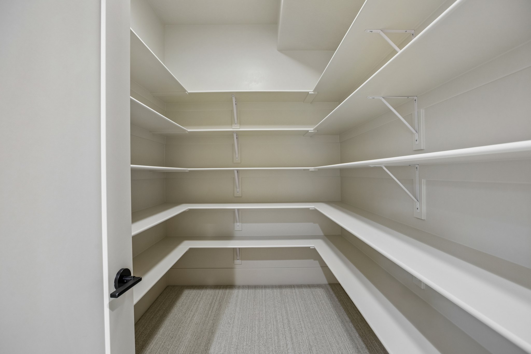 Walk-in pantry featuring extensive built-in shelving, durable white finishes, and light-toned flooring