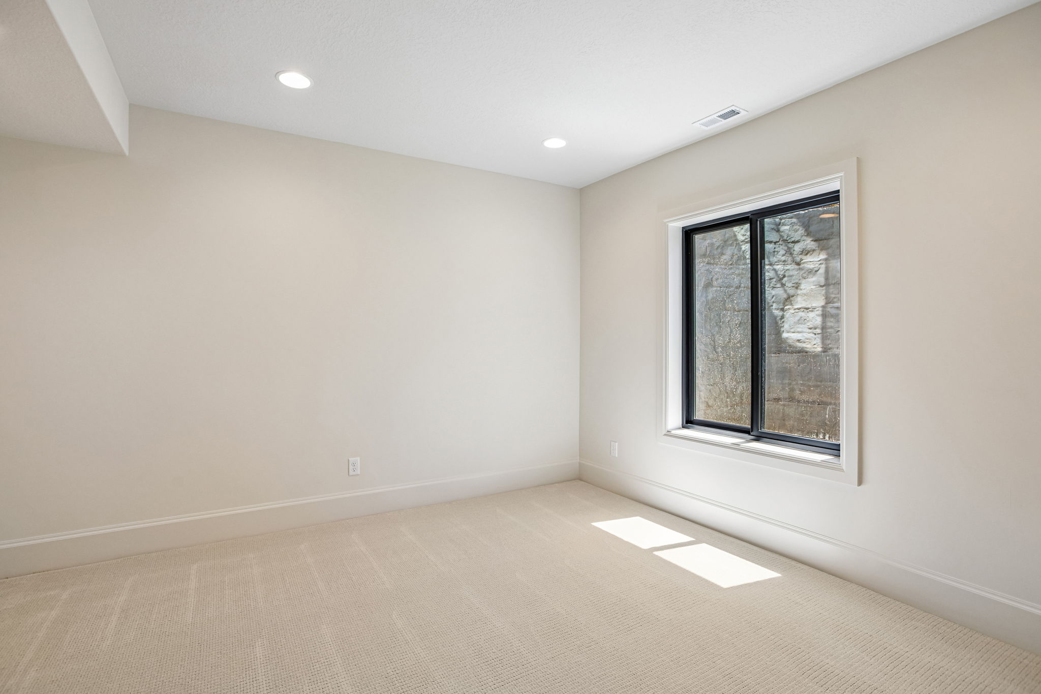 Carpeted interior space featuring neutral wall tones, recessed lighting, and a single window with a black frame