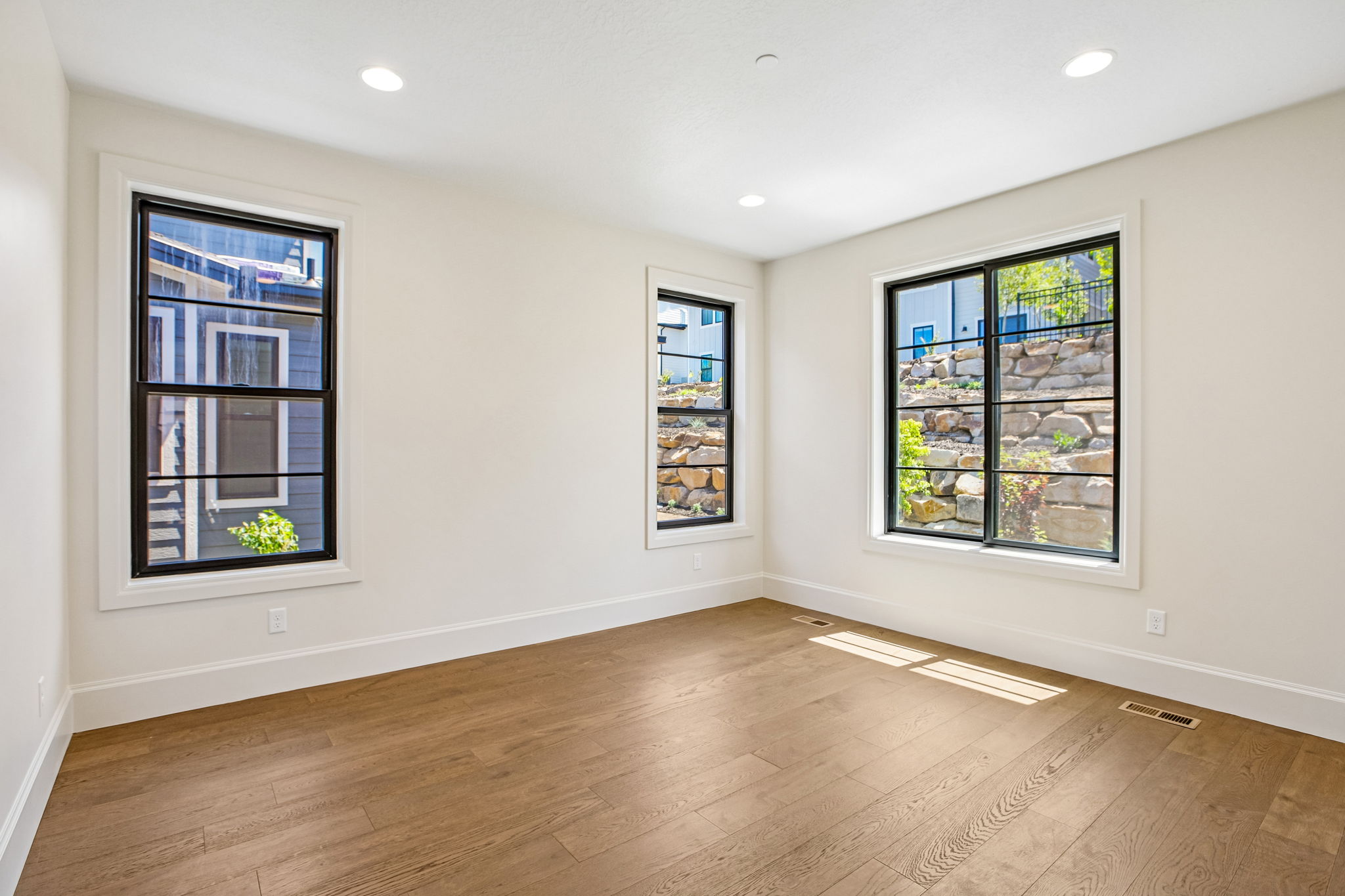 Spacious room featuring wood-finish flooring, recessed lighting, and multiple large black-framed windows