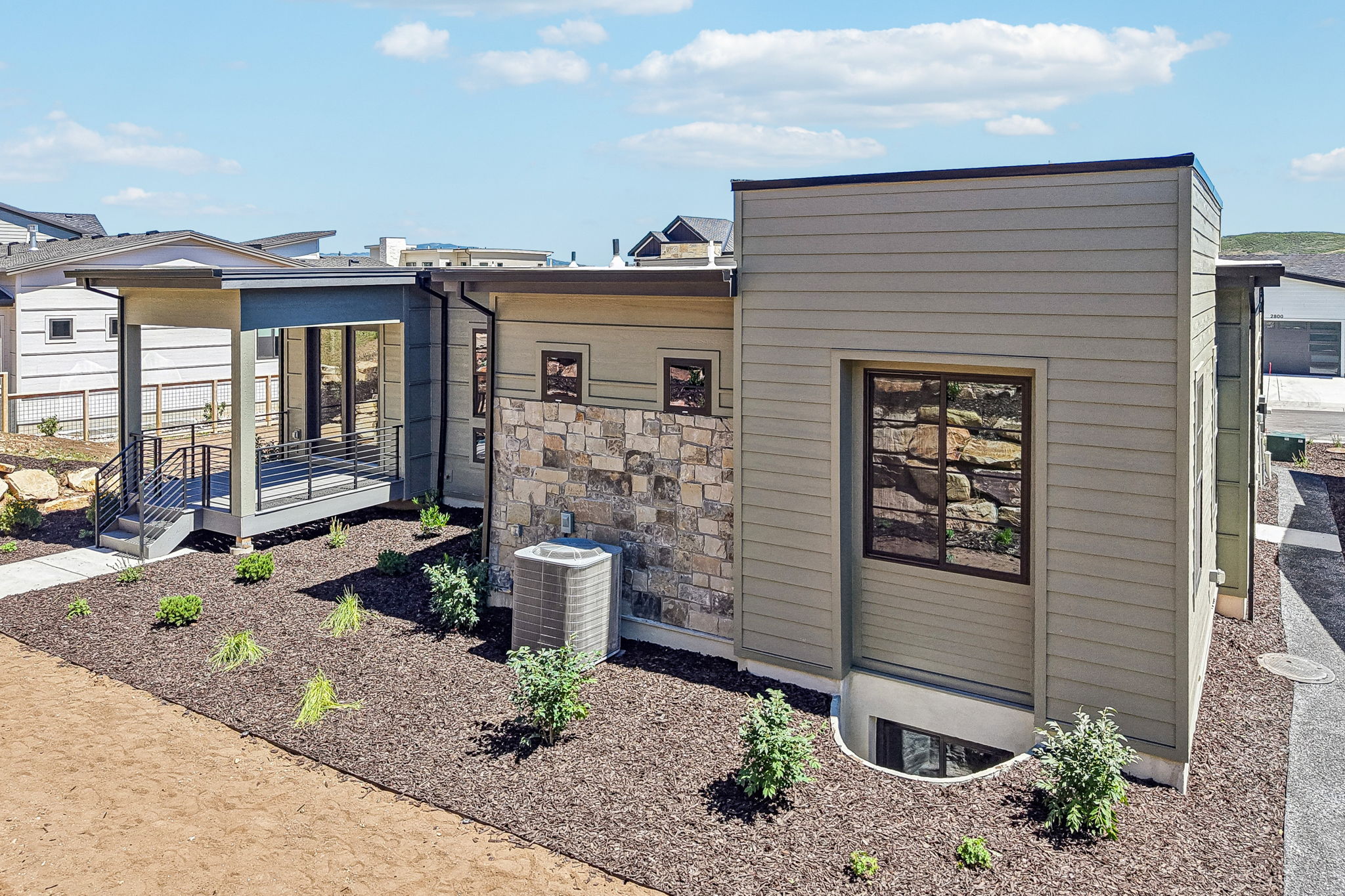 Modern exterior featuring horizontal siding, stone accents, a covered patio with dark railings, a concrete pathway, and a landscaped bed with mulch and plantings