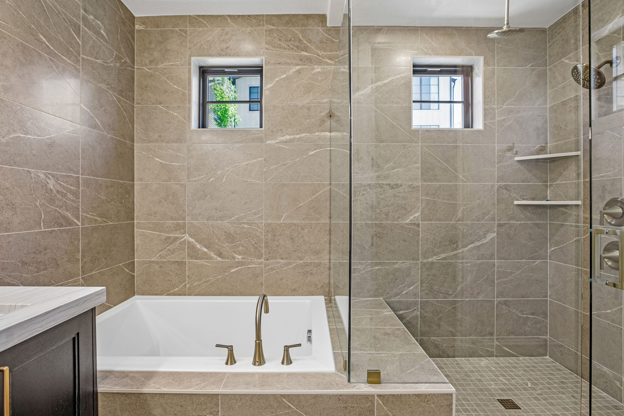 Bathroom featuring a built-in tub, walk-in shower with glass enclosure, two recessed windows, and full-height stone-look tile