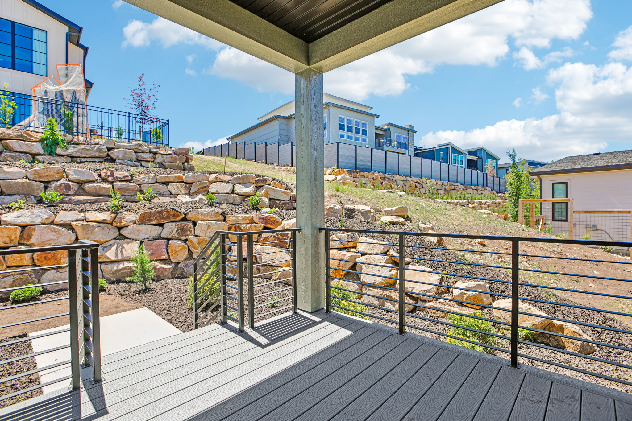 Covered deck featuring composite decking, modern cable railing, and a stone retaining wall