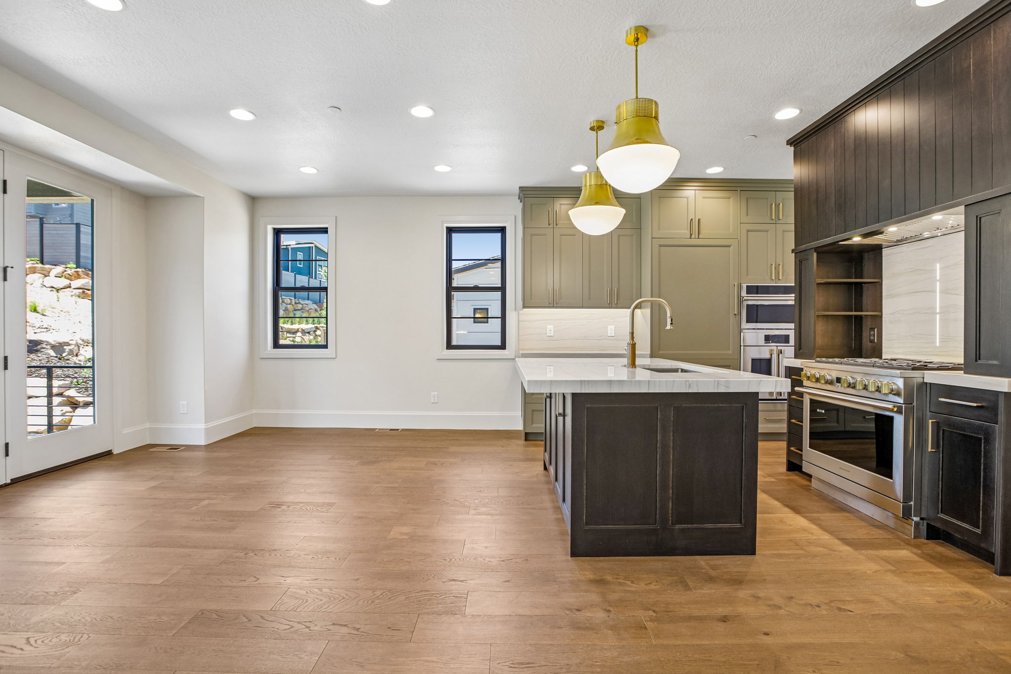 Open-concept kitchen and living area featuring wood-finish flooring, recessed lighting, a kitchen island with sink and brass faucet, stainless steel appliances, and a double glass door