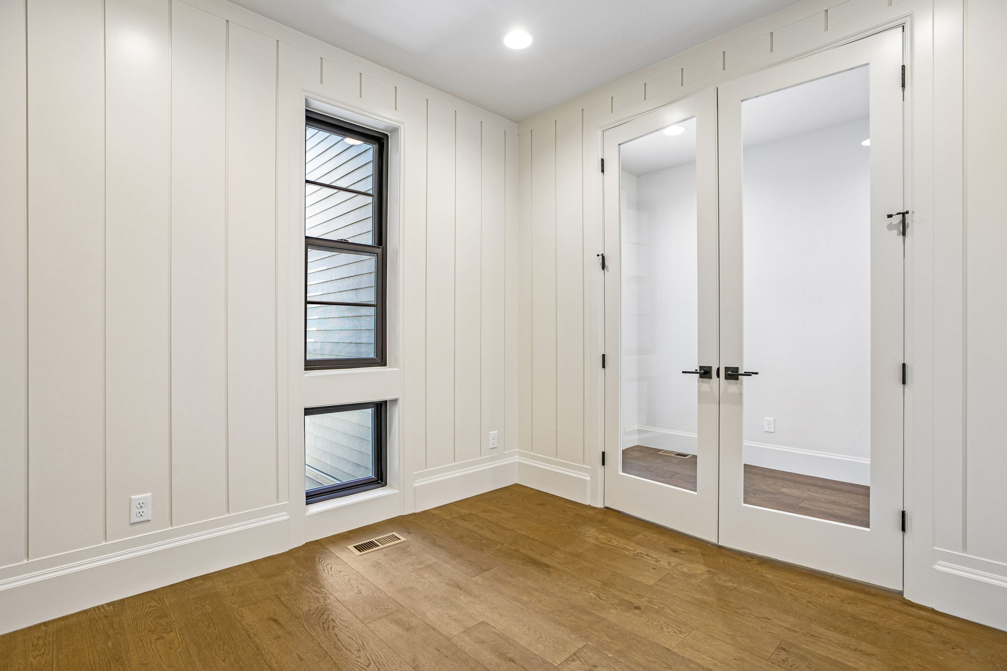 Room featuring wood-finish flooring, vertical paneling, and white baseboards