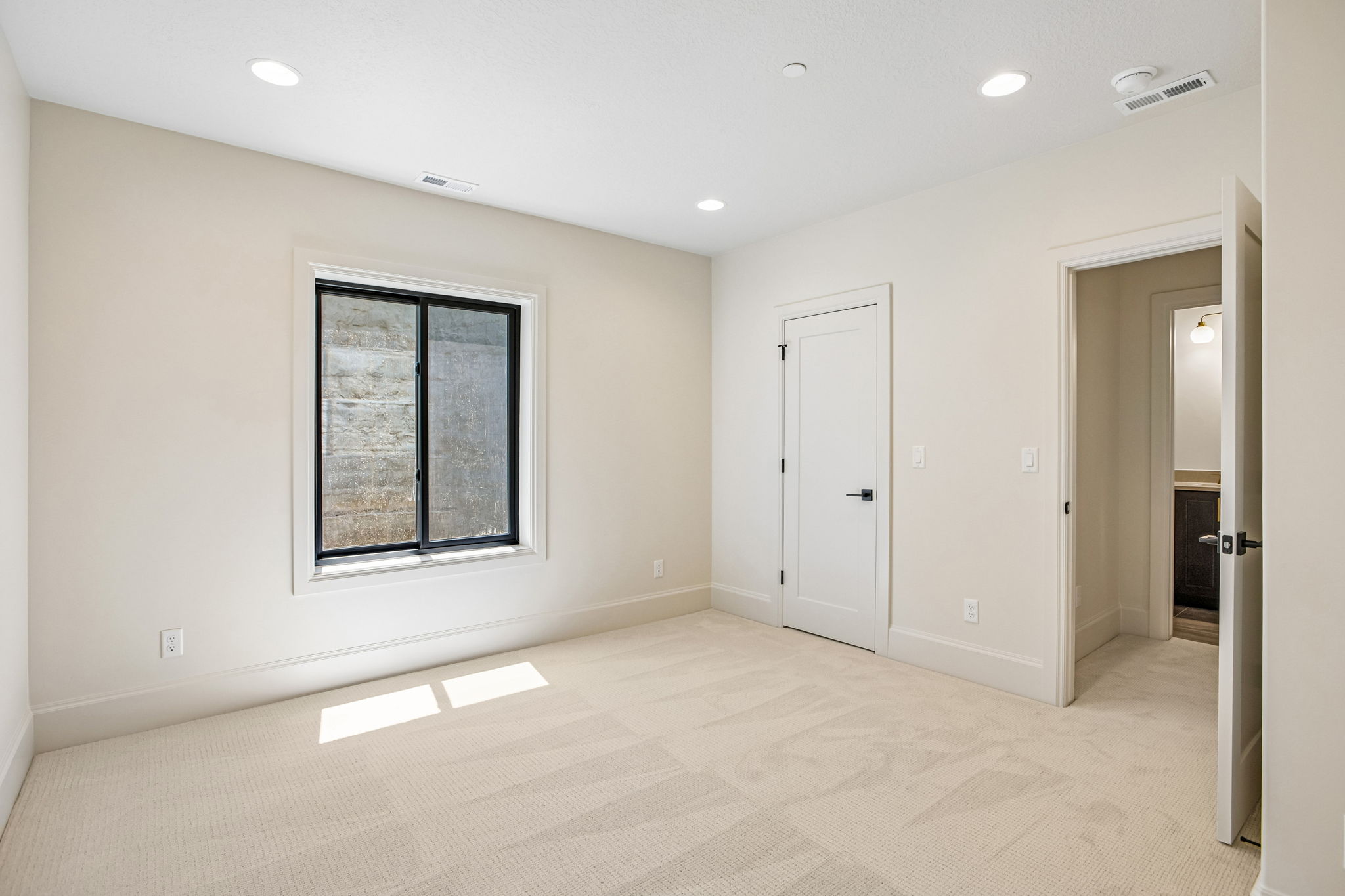 Neutral-toned room featuring a large window with black trim, recessed lighting, and light-colored carpeting