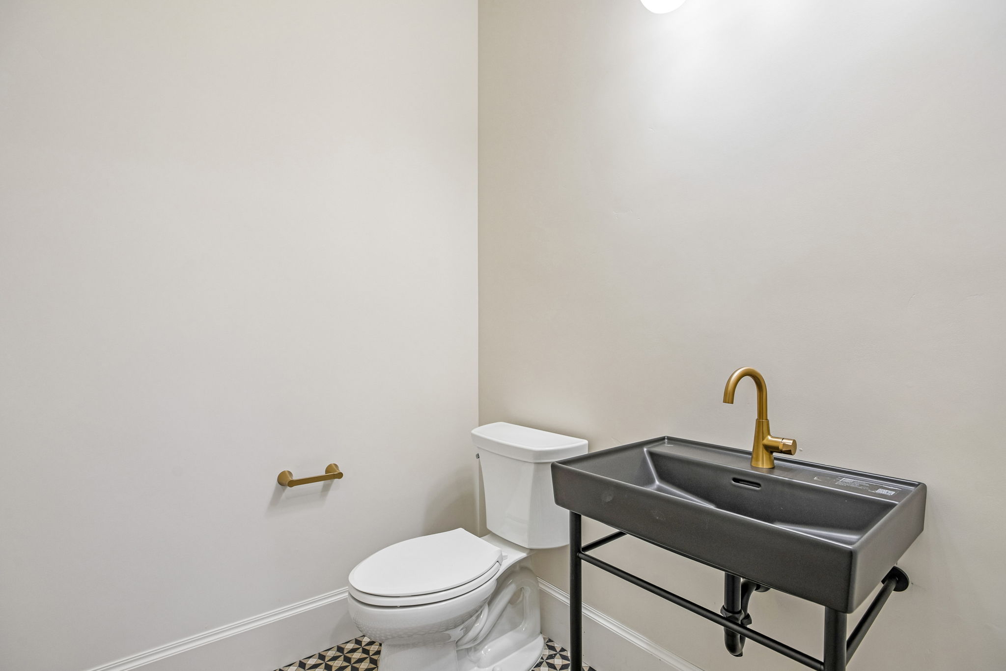 Modern powder room featuring a wall-mounted sink with a gold-tone faucet, white toilet, patterned floor tile, gold-tone toilet paper holder, and recessed lighting