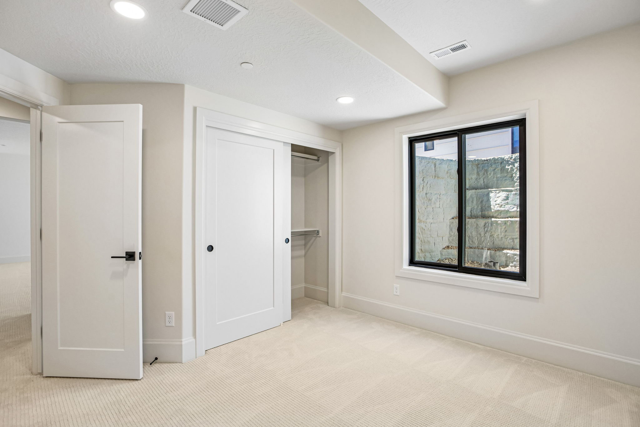 Neutral-toned room featuring recessed lighting, a sliding closet door, and a black-framed window with a window well