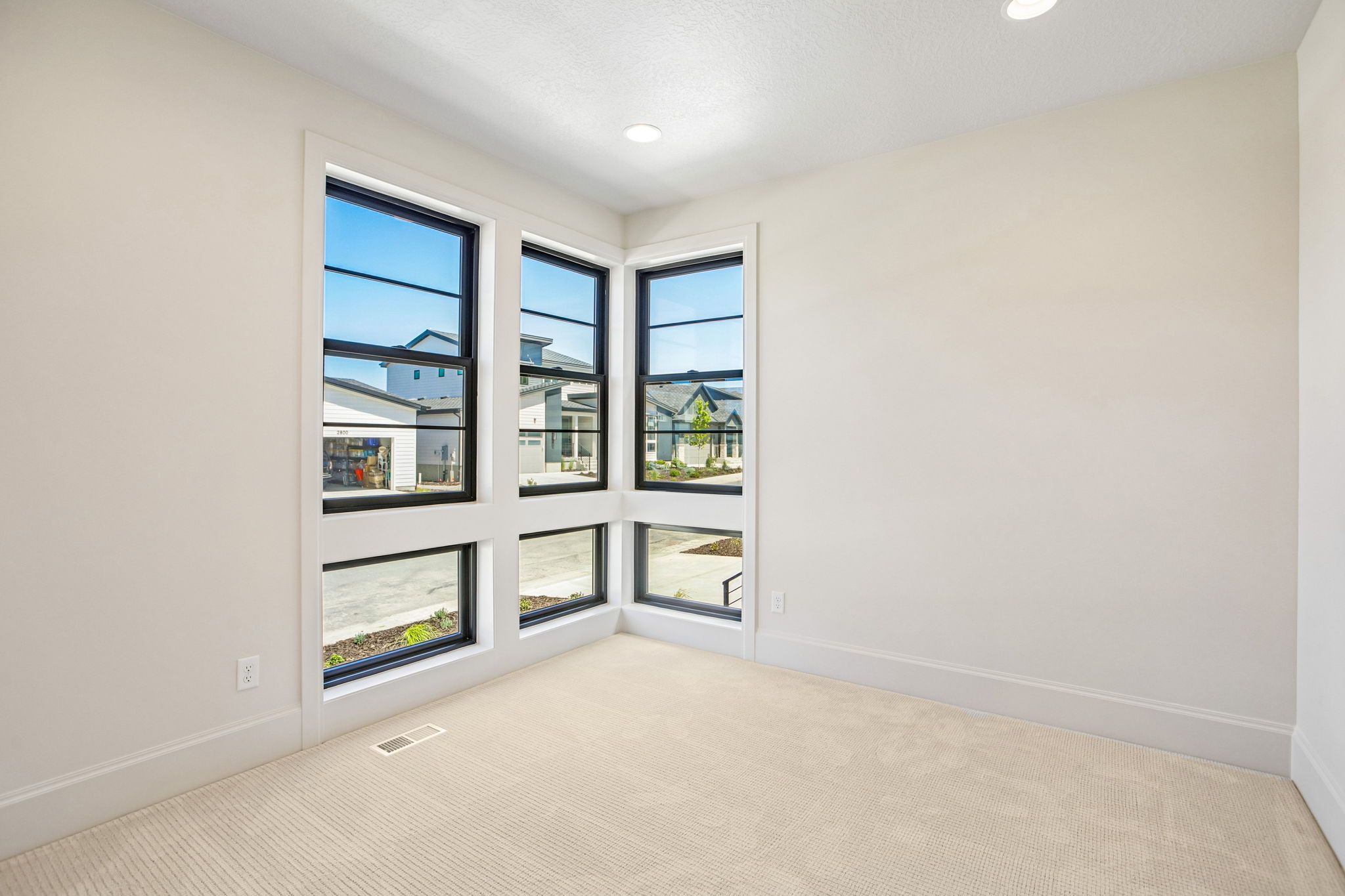 Corner window configuration with black frames, white trim, and light-colored carpeting