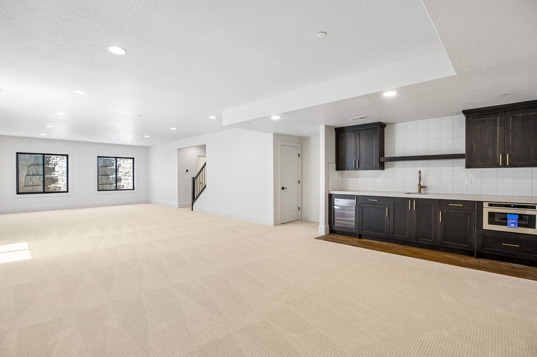 Spacious open-concept room featuring a built-in wet bar with dark cabinetry, integrated beverage refrigerator, microwave, and light-toned countertops