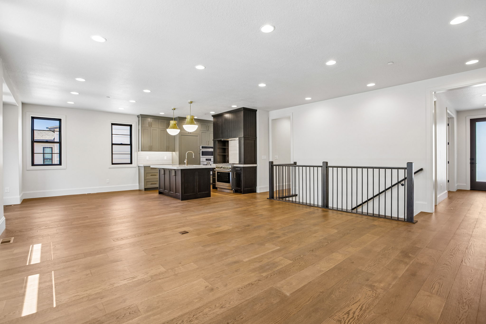 Expansive room featuring wood-finish flooring, recessed lighting, and a kitchen area with an island, pendant lighting, and stainless steel appliances