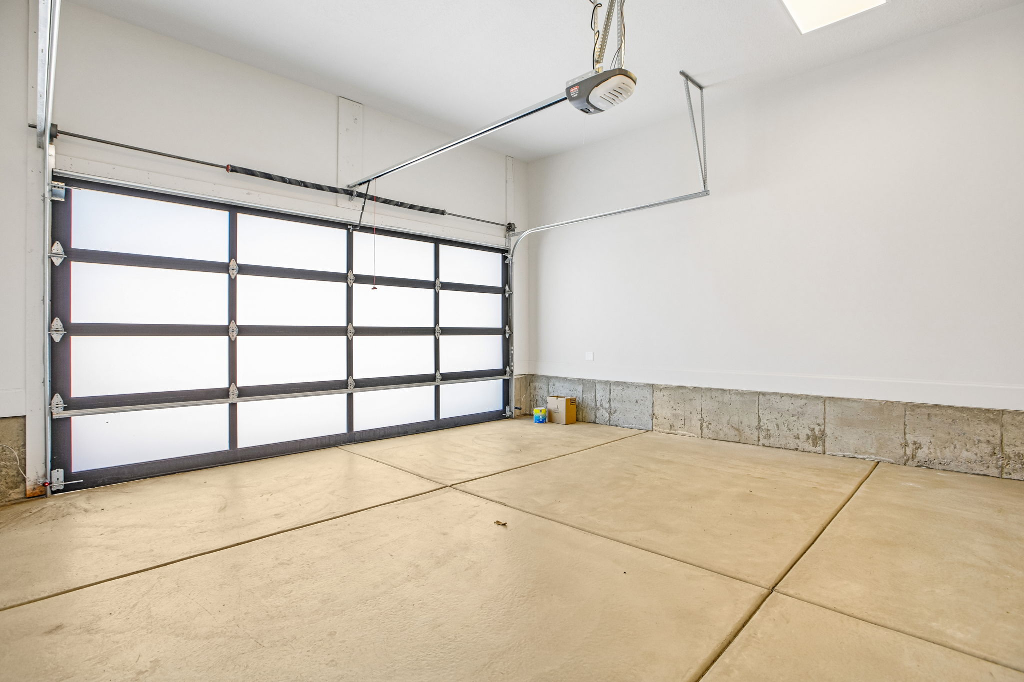 Garage interior featuring a sectional glass-paneled door, automatic opener, concrete flooring, and light-colored walls