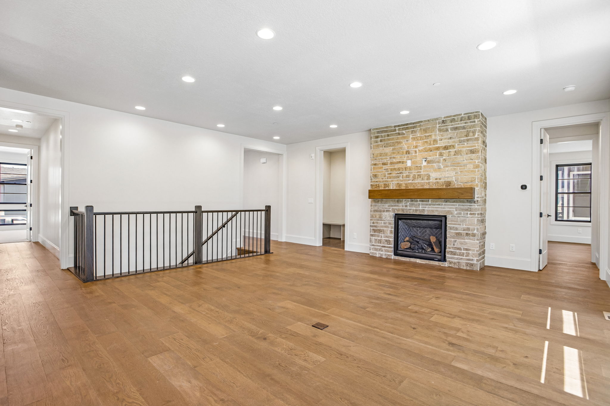 Interior living space featuring wood-finish flooring, a stone-clad fireplace with a wood mantle, recessed lighting, and a black metal spindle railing