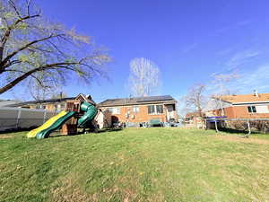 Rear view of property featuring a fenced backyard, roof mounted solar panels, and a playground