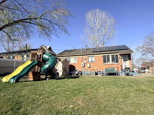 Rear view of house with a storage shed, solar panels, brick siding, and a playground