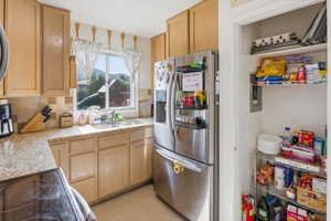 Light-toned wood cabinetry with a tile backsplash, light-colored countertops, stainless steel appliances, and a double-basin sink
