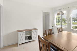 Dining area featuring light-colored tile flooring, multiple windows with white sheer curtains, and a white built-in cabinet with a wood-finish countertop