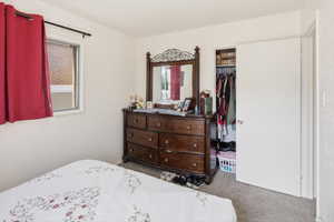 Carpeted bedroom featuring a window, painted white walls, and a closet with a bi-fold door