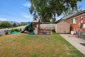 Expansive rear yard featuring a wooden playset with a green slide and swing set, a detached storage shed, and a concrete patio area