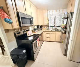 Kitchen featuring light wood finish cabinetry, stainless steel appliances, a textured ceiling, light tile patterned floors, and decorative backsplash