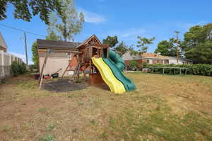 Spacious backyard featuring a wooden playset with two slides, a dedicated swing set area, and a storage shed