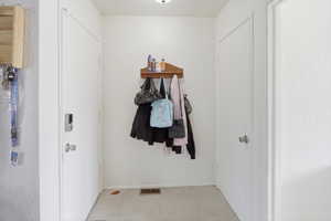 Entryway featuring two white doors, a light tile floor, and a wall-mounted wooden shelf
