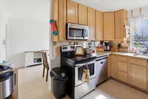 Kitchen featuring light wood cabinetry, granite-style countertops, stainless steel appliances, and a tile backsplash
