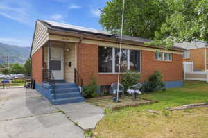 Brick and siding exterior featuring solar panels, a covered entry with metal railings, a concrete driveway, and established landscaping
