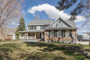 View of front of house with a porch, a front lawn, brick siding, and roof with shingles